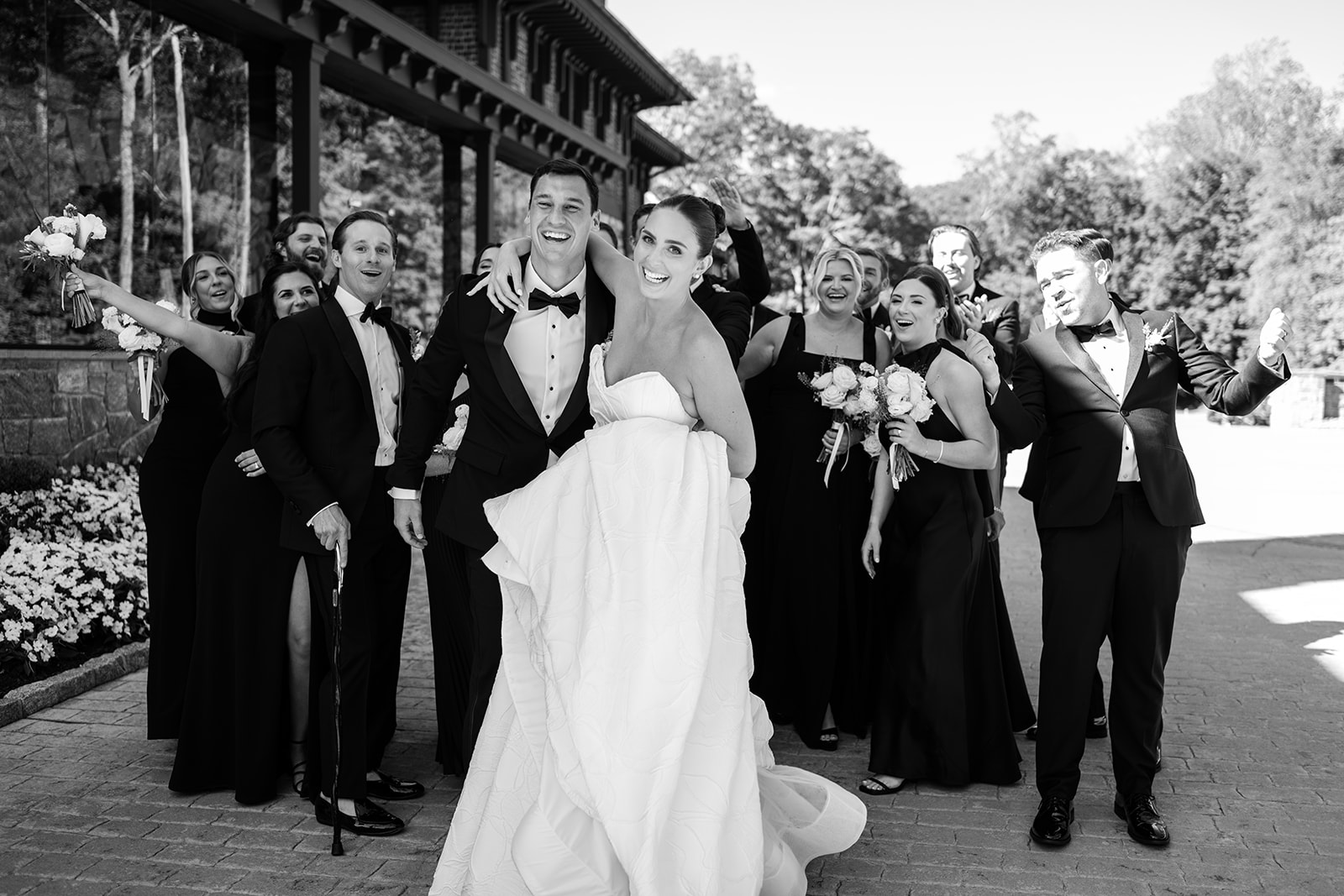 Black and white film photo of the couple laughing as they lead their wedding party on a walk.